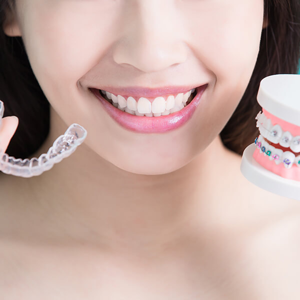 Woman holding up clear aligners and braces