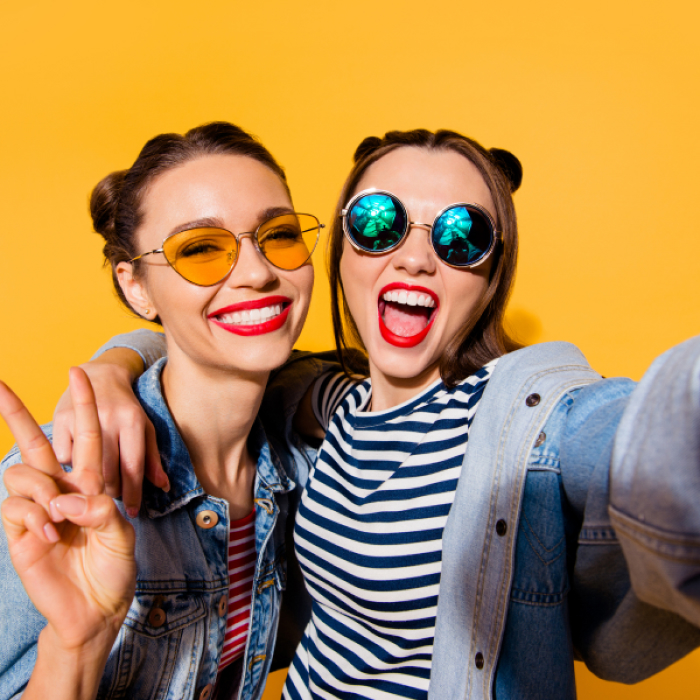 Two young women wearing sunglasses smile for a selfie